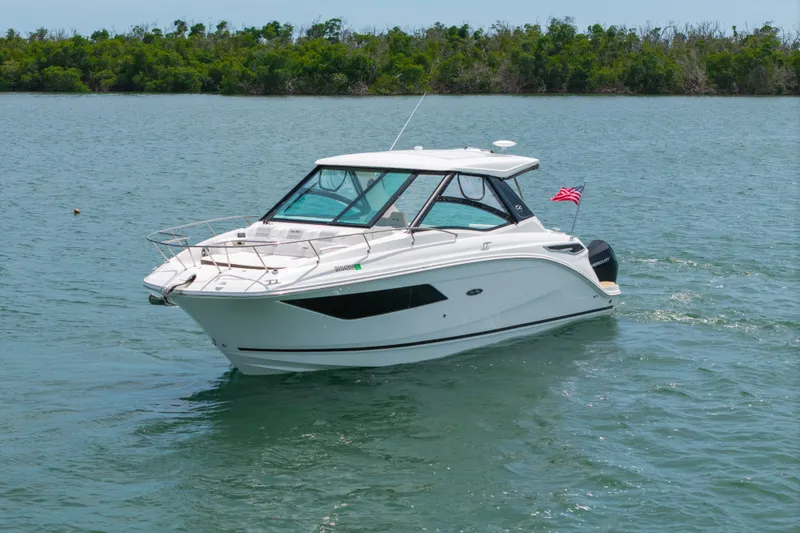 Slide: The Image of 2024 Sea Ray Sundancer 320 Outboard cruising on a serene lake with lush greenery. - 10