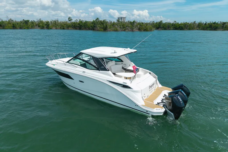 Slide: The Image of 2024 Sea Ray Sundancer 320 Outboard cruising on a serene lake under a clear sky. - 11