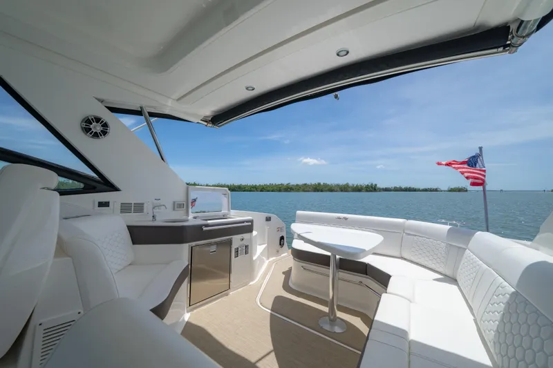 Slide: The Image of 2024 Sea Ray Sundancer 320 Outboard interior with seating, table, and American flag on water. - 21