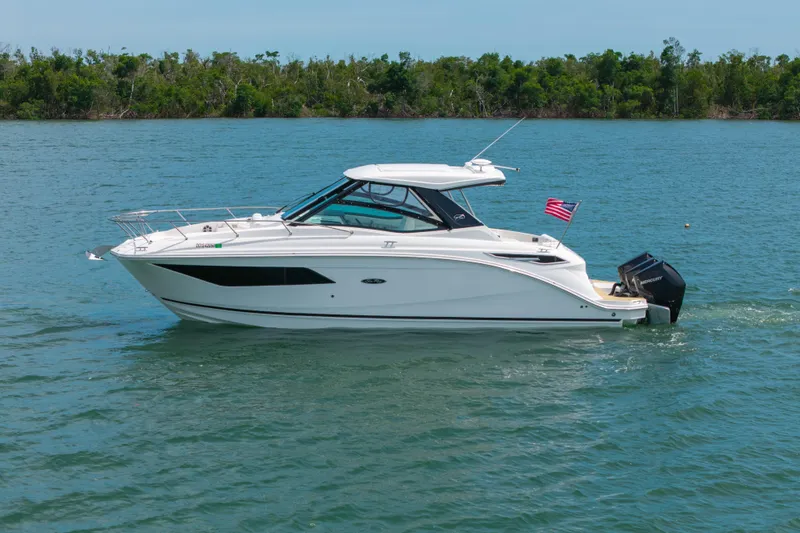 Slide: The Image of 2024 Sea Ray Sundancer 320 Outboard cruising on a serene lake with lush green shoreline. - 8
