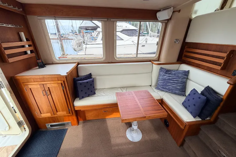 Slide: The Image of Cozy interior of 2002 American Tug 34 with white seating, wooden table, and marina view. - 7