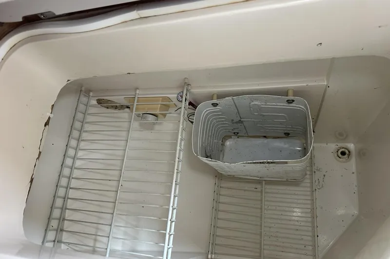 Slide: The Image of Empty refrigerator compartment in a 1991 Catalina 42 boat, showing wire shelf and container. - 57