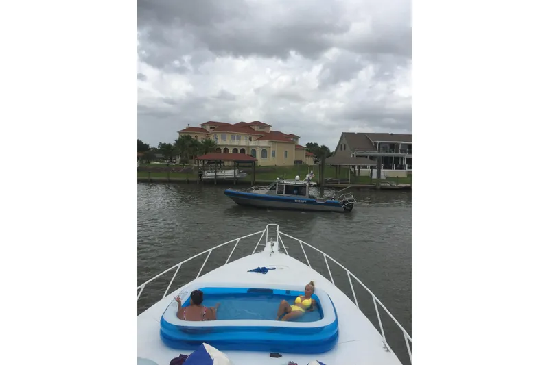 Slide: The Image of 1994 Breaux Bay Craft 58 Sportfish with onboard pool, cruising near waterfront homes under cloudy skies. - 10