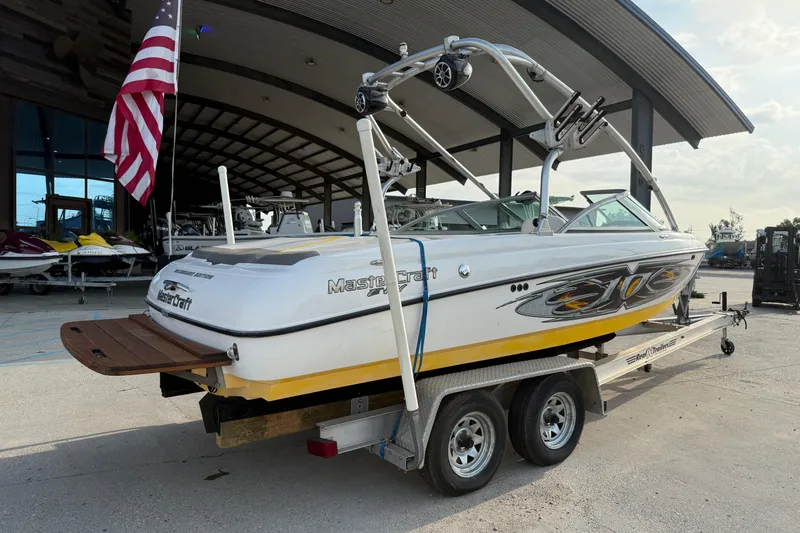 Slide: The Image of 2005 MasterCraft X10 boat on trailer, parked near a building with an American flag. - 3