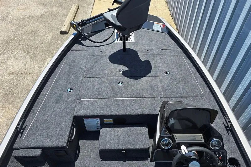 Slide: The Image of 2026 Lowe Stinger 175 boat interior with steering console and seating, docked near metal siding. - 3