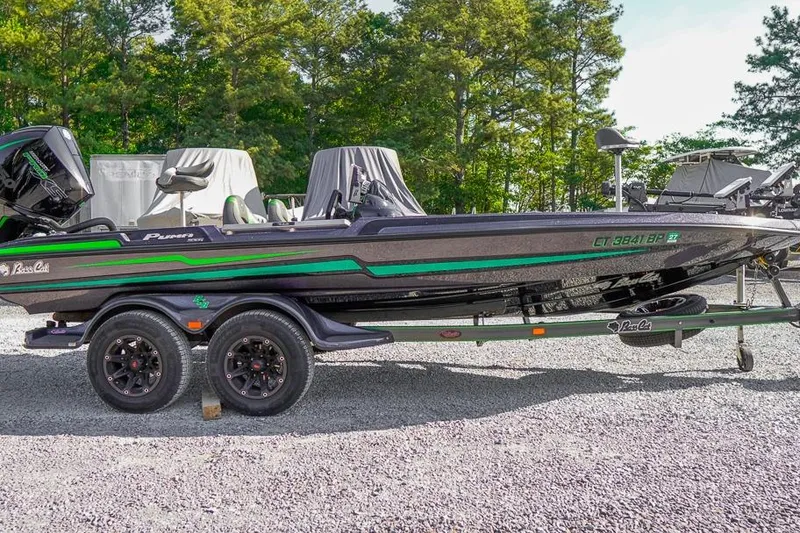 The Image of 2023 Bass Cat Puma STS boat with green accents on a trailer, parked outdoors. - 1