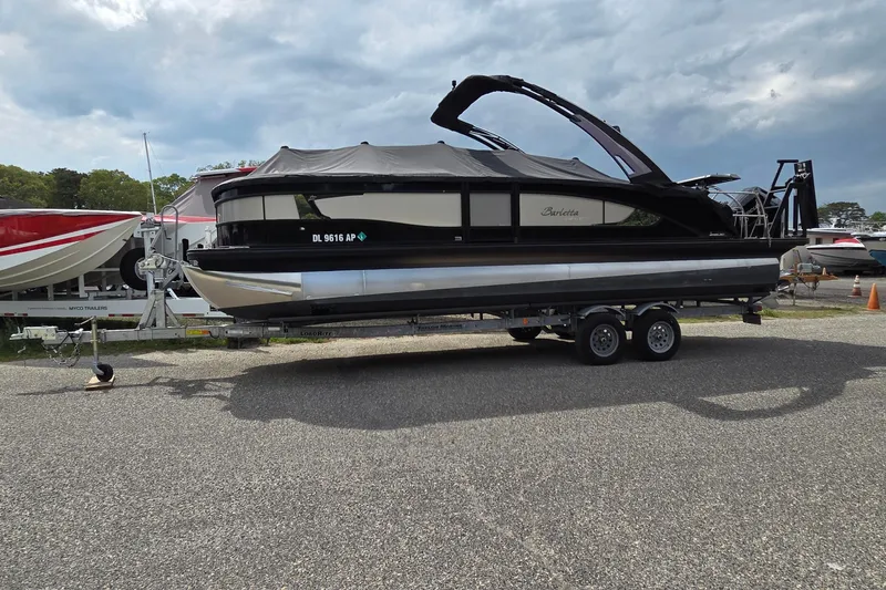 Slide: The Image of 2025 Barletta Lusso 25UCA pontoon boat on a trailer, parked outdoors. - 22