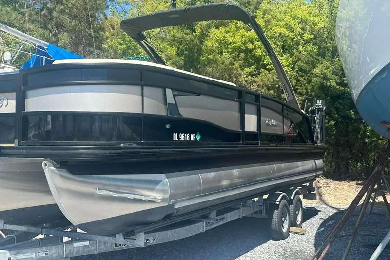 Slide: The Image of 2025 Barletta Lusso 25UCA pontoon boat on trailer, surrounded by trees. - 24