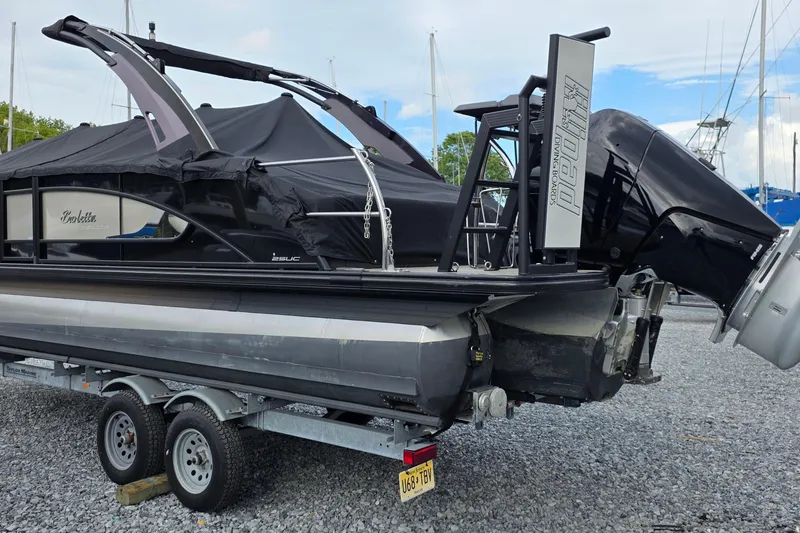 Slide: The Image of 2025 Barletta Lusso 25UCA pontoon boat on trailer, covered and parked on gravel. - 3