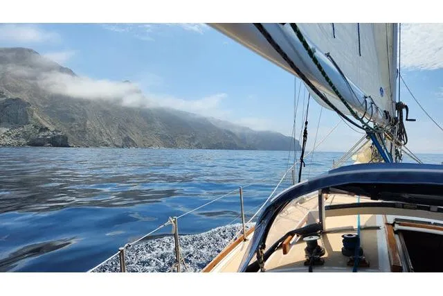 Slide: The Image of Sailing on a 1982 Cape Dory 36 near rocky coastline under clear skies. - 60