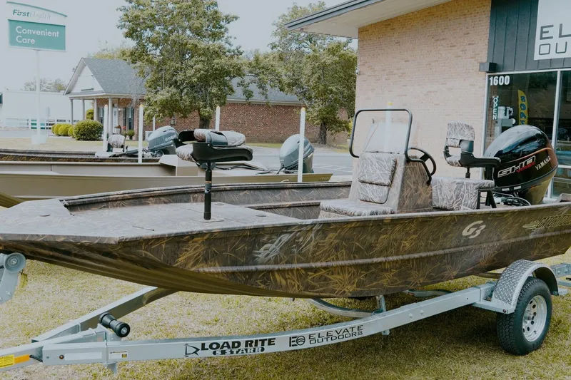 The Image of 2026 G3 Gator Tough 18 CC boat on trailer, camo design, parked outdoors. - 1