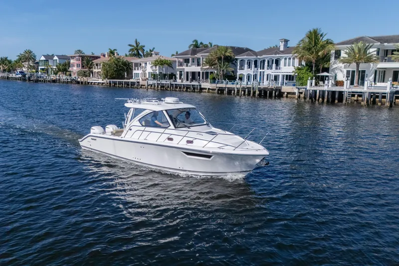 Slide: The Image of 2018 Pursuit OS 325 Offshore boat cruising near waterfront homes on a sunny day. - 2