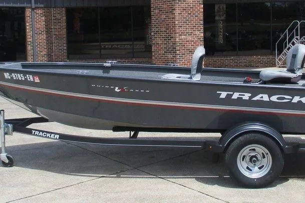 The Image of A Tracker boat on a trailer, parked outside a brick building. - 1