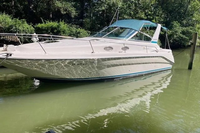 Slide: The Image of 1994 Sea Ray 290 Sundancer boat docked on calm water, surrounded by lush greenery. - 9
