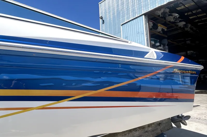 Slide: The Image of 2007 Sunsation 32 Dominator boat with blue, orange, and white design near a storage facility. - 3