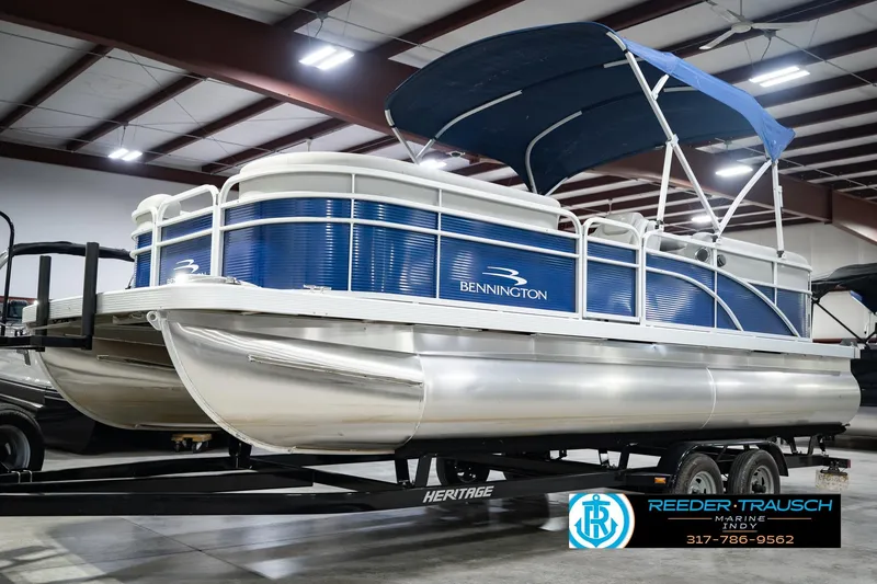 Slide: The Image of 2021 Bennington 22 SVSR pontoon boat with blue canopy on trailer in showroom. - 2
