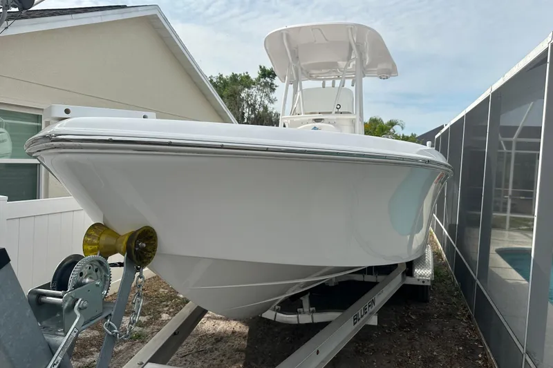 Slide: The Image of 2024 Aquasport 230 Pro Bay boat on trailer, parked beside a house. - 2