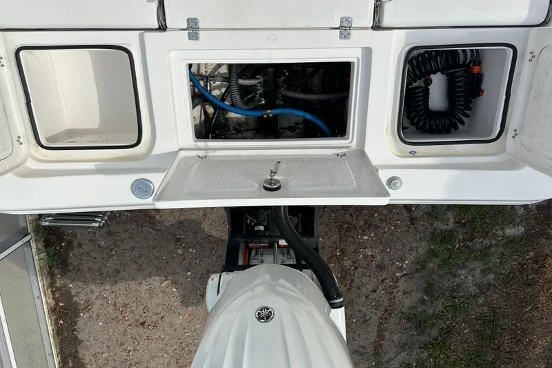 Slide: The Image of 2024 Aquasport 230 Pro Bay boat engine compartment with storage and coiled hose. - 20