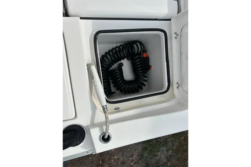 Slide: The Image of 2024 Aquasport 230 Pro Bay boat storage compartment with coiled hose. - 22