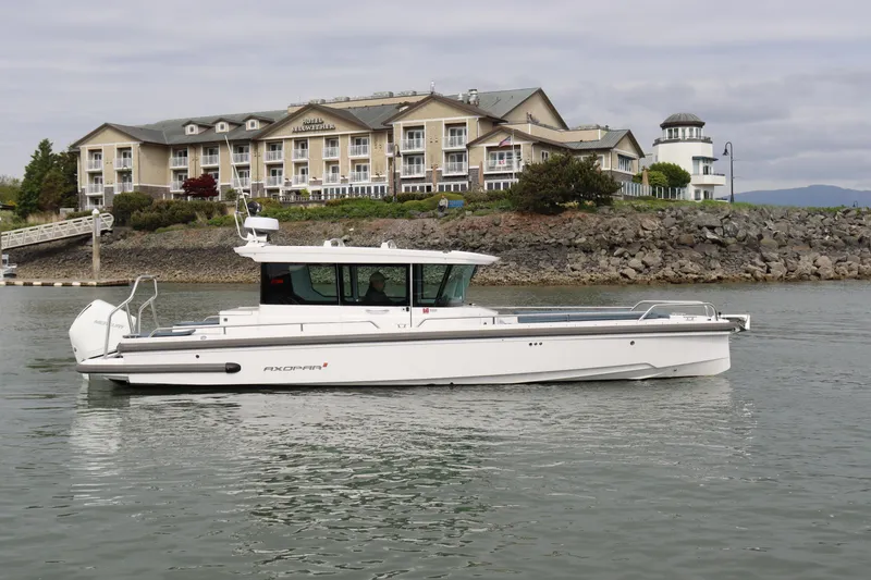 The Image of 2022 Axopar 28 Cabin boat on water near a hotel and rocky shoreline. - 0