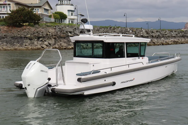Slide: The Image of 2022 Axopar 28 Cabin boat cruising near rocky shoreline with lighthouse in background. - 2