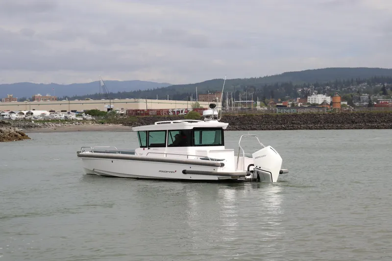 Slide: The Image of 2022 Axopar 28 Cabin boat cruising in a harbor with industrial backdrop. - 3