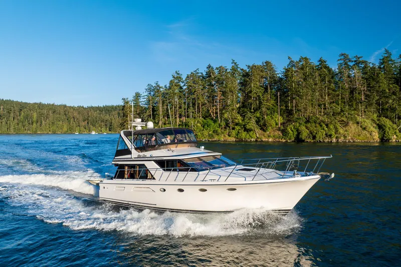 The Image of 1990 Ocean Alexander 48 Sedan cruising on a scenic waterway with lush forest backdrop. - 0