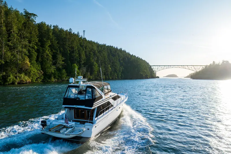 Slide: The Image of 1990 Ocean Alexander 48 Sedan cruising through scenic waterway with bridge and forest backdrop. - 4