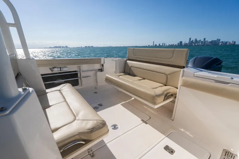 Slide: The Image of 2018 Pursuit S 328 Sport boat interior with beige seating, ocean view, and city skyline. - 27