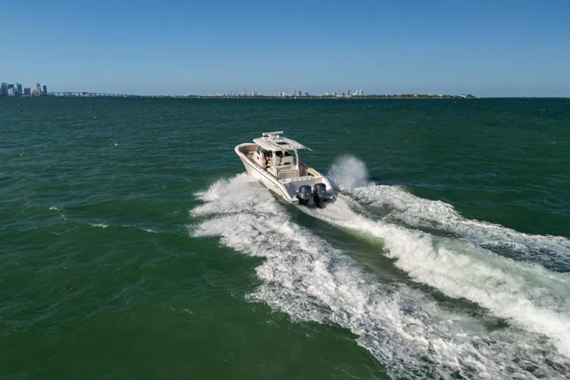 Slide: The Image of 2018 Pursuit S 328 Sport boat cruising on open water with city skyline in background. - 8