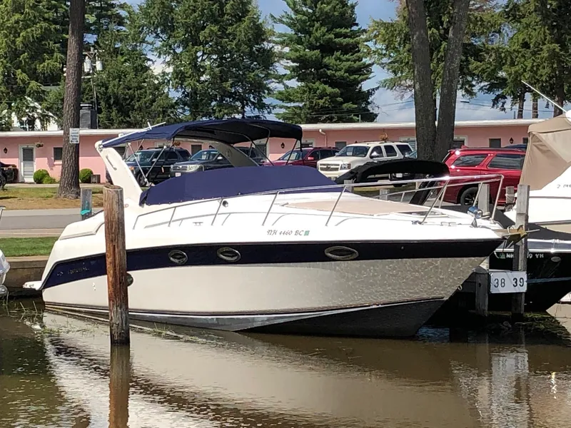 The Image of 1999 Regal 322 Commodore boat docked in a marina with trees and cars in the background. - 0
