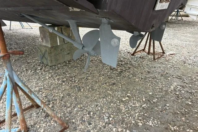 Slide: The Image of 2001 Wellcraft 3300 Martinique boat propellers and rudders on gravel, supported by stands. - 3