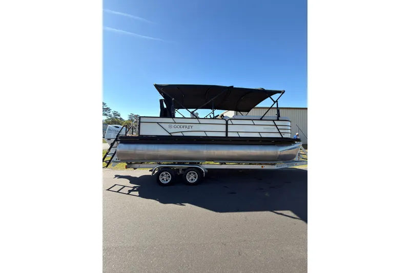 The Image of 2021 Godfrey 2286 pontoon boat on trailer under clear blue sky. - 0