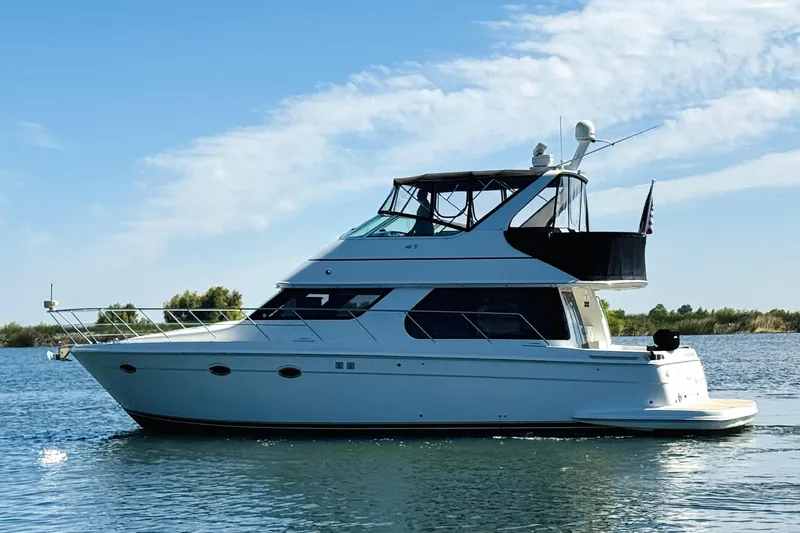 Slide: The Image of 2006 Carver 46 Voyager yacht cruising on a serene lake under a clear blue sky. - 9