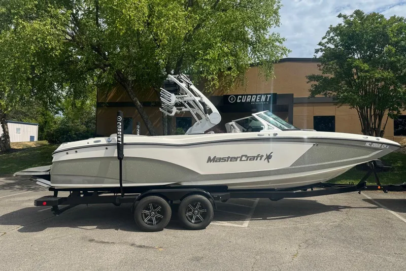 The Image of 2017 MasterCraft X26 boat on trailer, parked outdoors near trees and building. - 0
