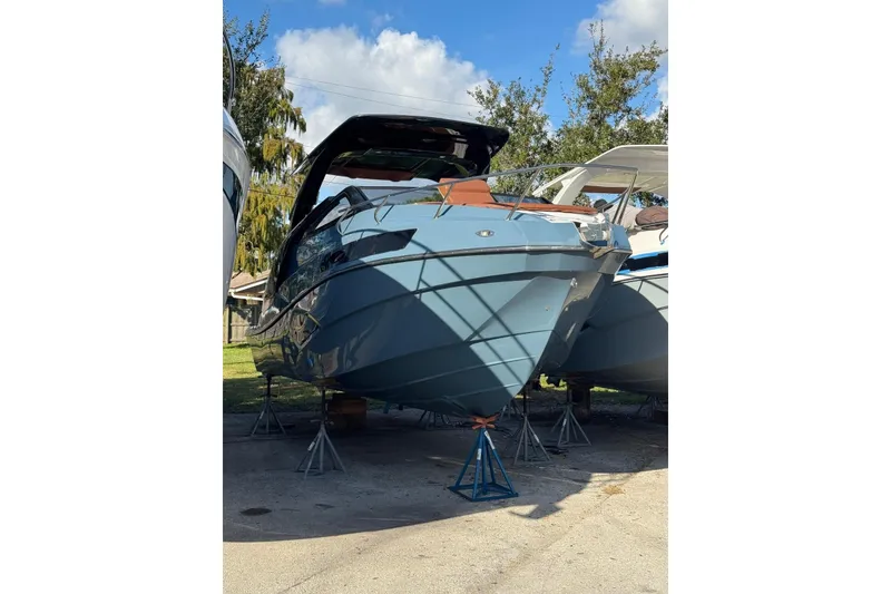 Slide: The Image of 2025 NX Boats NX290 Exclusive on stands, blue hull, sunny day, trees in background. - 12