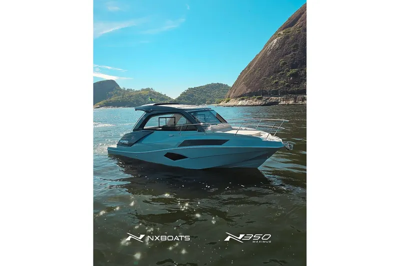 Slide: The Image of 2025 NX Boats NX350 MAXIMUS cruising on scenic waterway with mountainous backdrop. - 22