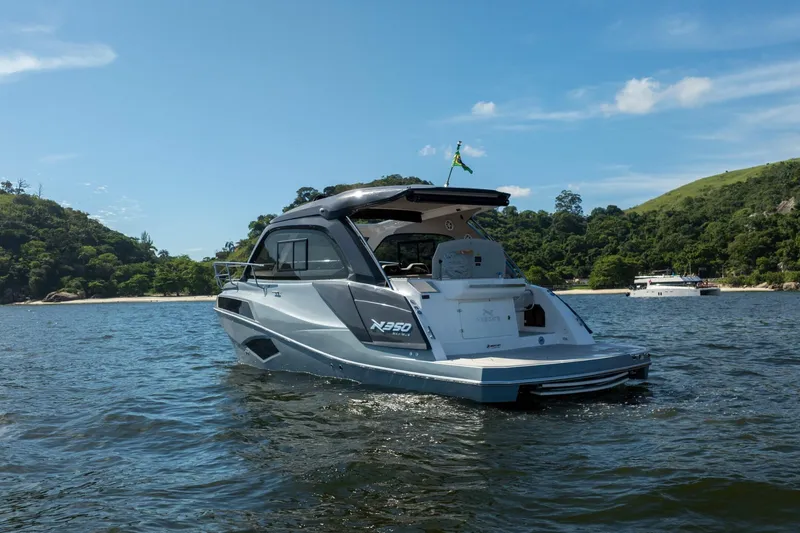 Slide: The Image of 2025 NX Boats NX350 MAXIMUS cruising on a scenic lake with lush green hills. - 7