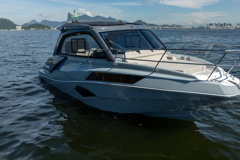 Slide: The Image of 2025 NX Boats NX350 MAXIMUS cruising on a scenic waterway with city skyline backdrop. - 9