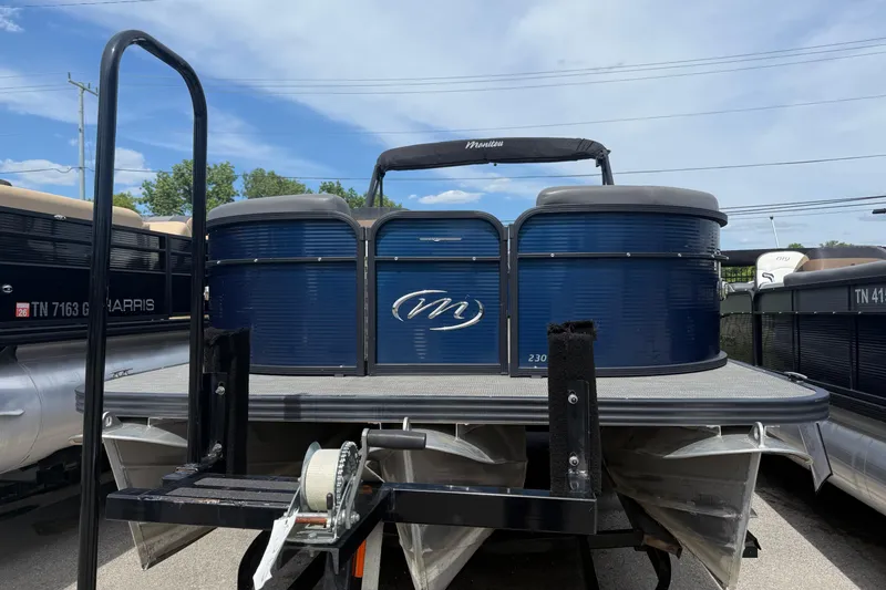 Slide: The Image of 2022 Manitou Aurora LE pontoon boat in blue, displayed on a trailer under a clear sky. - 1