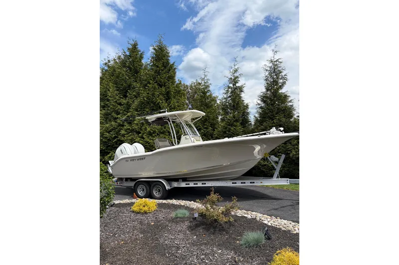 The Image of 2024 Key West 244 Center Console boat on trailer, surrounded by trees and cloudy sky. - 0