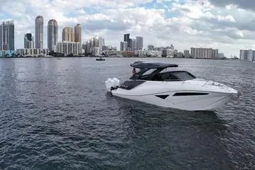 Slide: The Image of 2025 NX Boats NX360 Sport Coupe cruising on urban waterfront with skyscrapers in background. - 7