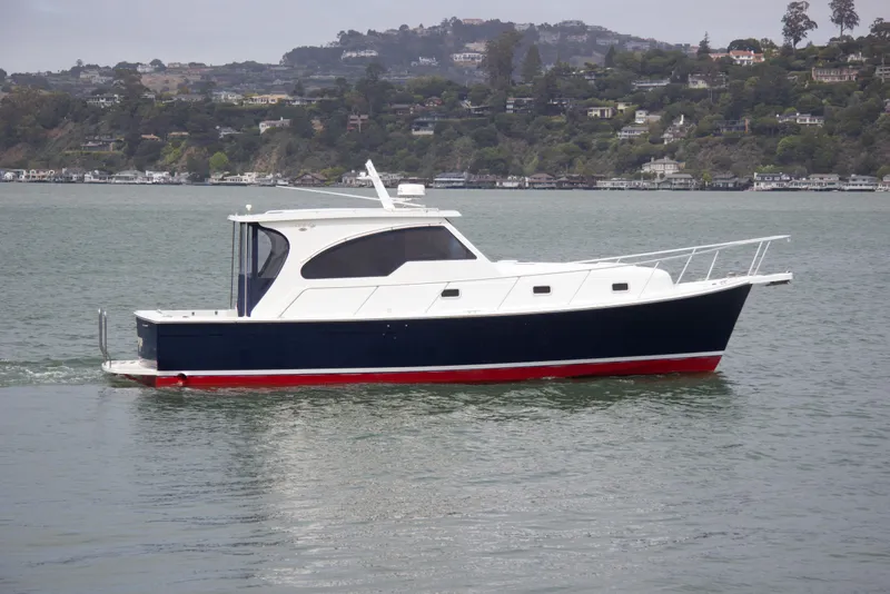 Slide: The Image of 2001 Mainship Pilot 34 Sedan cruising on a scenic lake with hillside homes. - 1