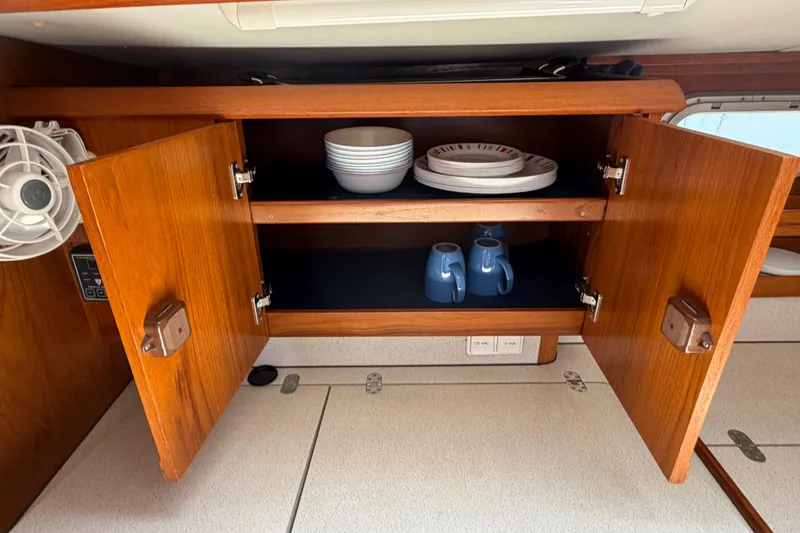 Slide: The Image of Open wooden cabinet in Jeanneau Sun Odyssey 45.2 yacht, displaying dishes and mugs. - 58