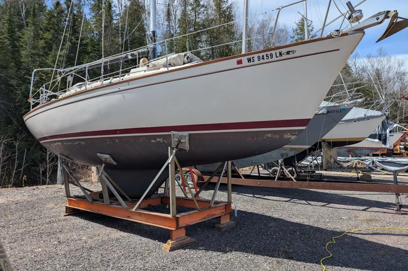 The Image of 1982 Pearson 323 sailboat on a stand, surrounded by trees and other boats. - 0
