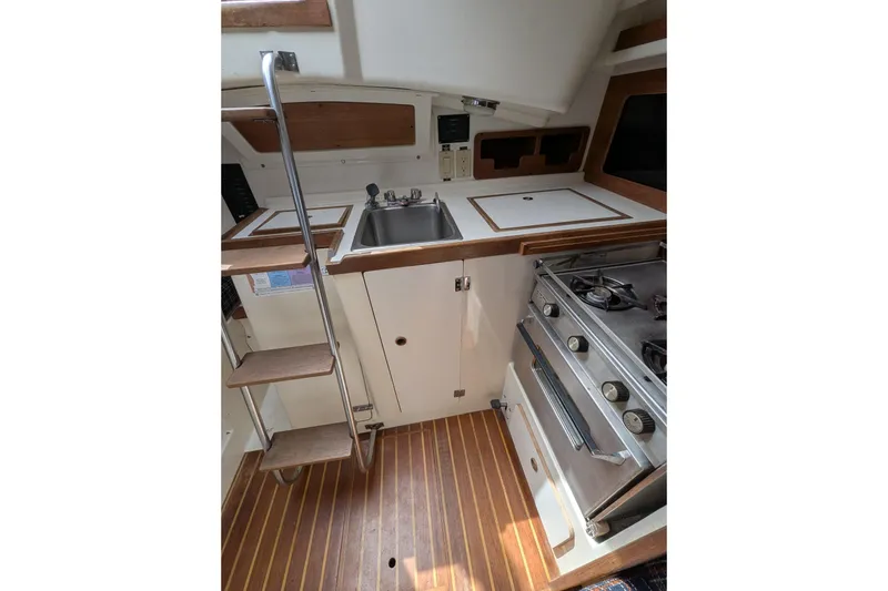 Slide: The Image of Compact kitchen area in a 1982 Pearson 323 sailboat with stove, sink, and wooden steps. - 13