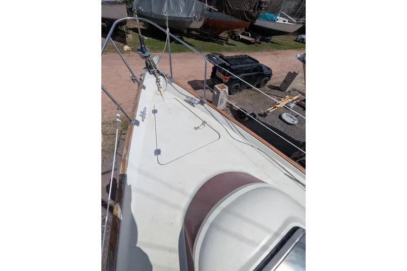 Slide: The Image of 1982 Pearson 323 sailboat deck with rigging, parked vehicles, and boats in the background. - 43