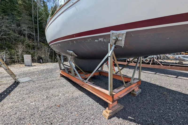 Slide: The Image of 1982 Pearson 323 sailboat on stands, gravel yard, forest background. - 53