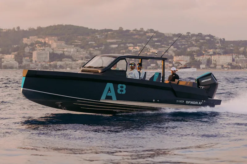 Slide: The Image of 2027 XO DFNDR 8 boat cruising on water with scenic coastal backdrop. - 15