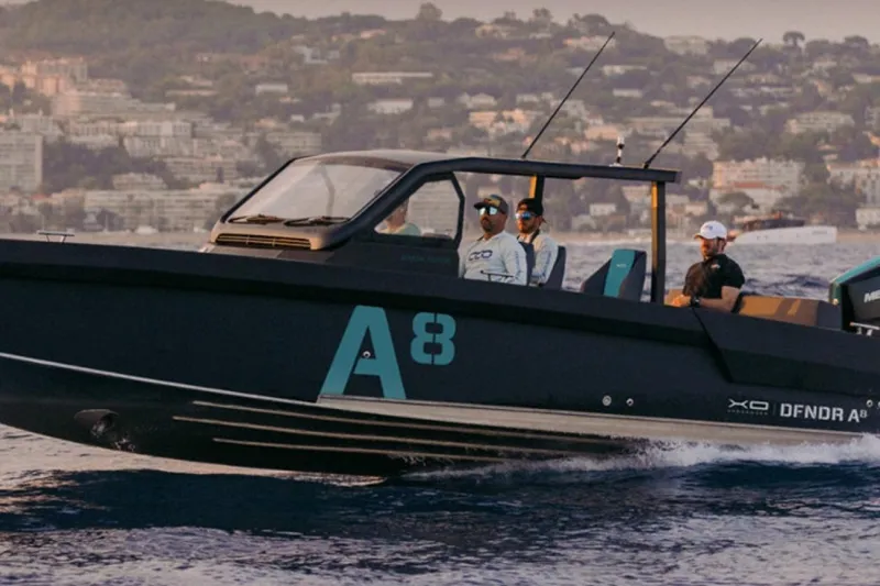 Slide: The Image of 2027 XO DFNDR 8 boat cruising on water with passengers, scenic coastal backdrop. - 4